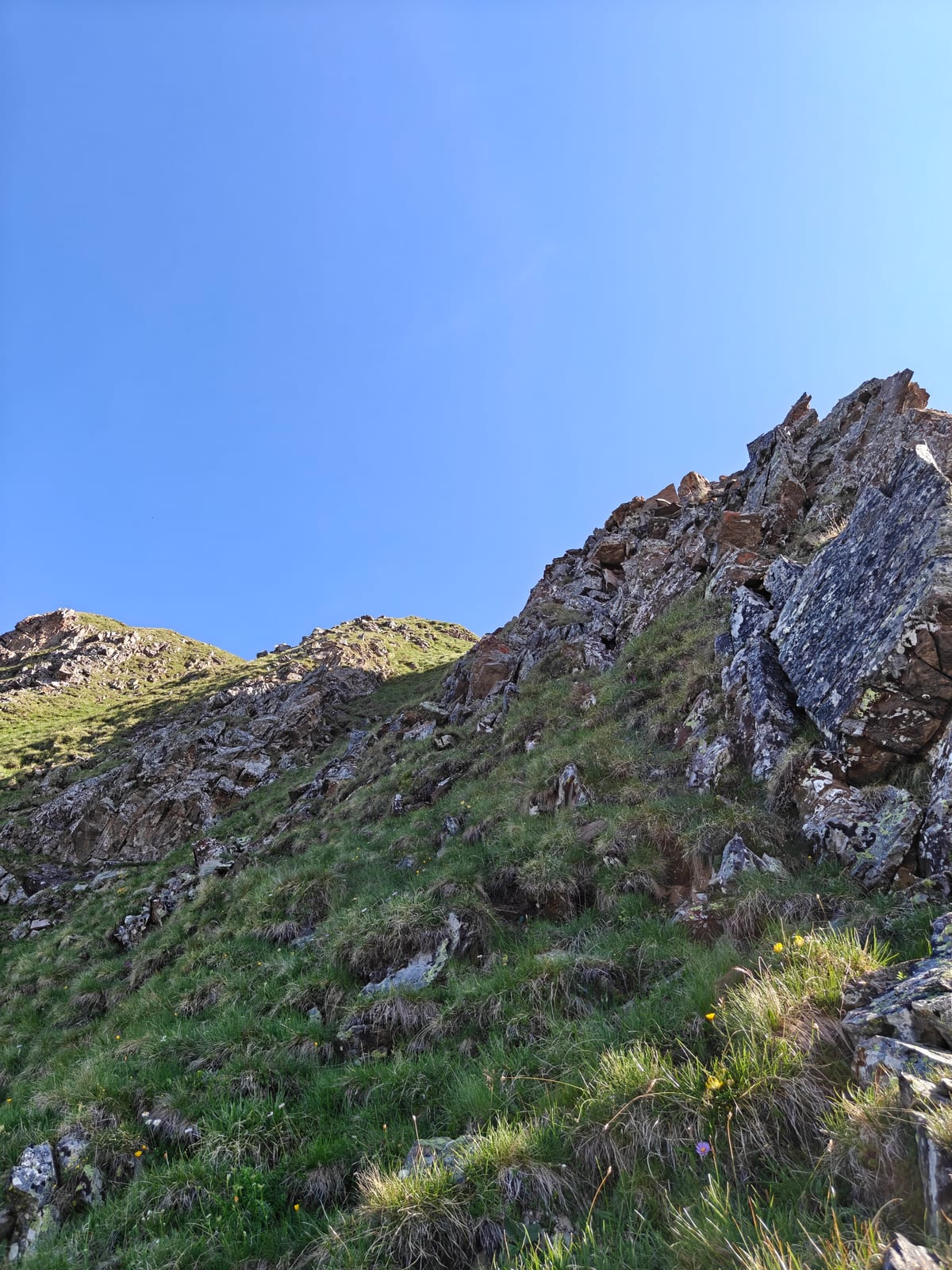 Steep grassy slope with rock outcrops, climbing toward a ridge crest
