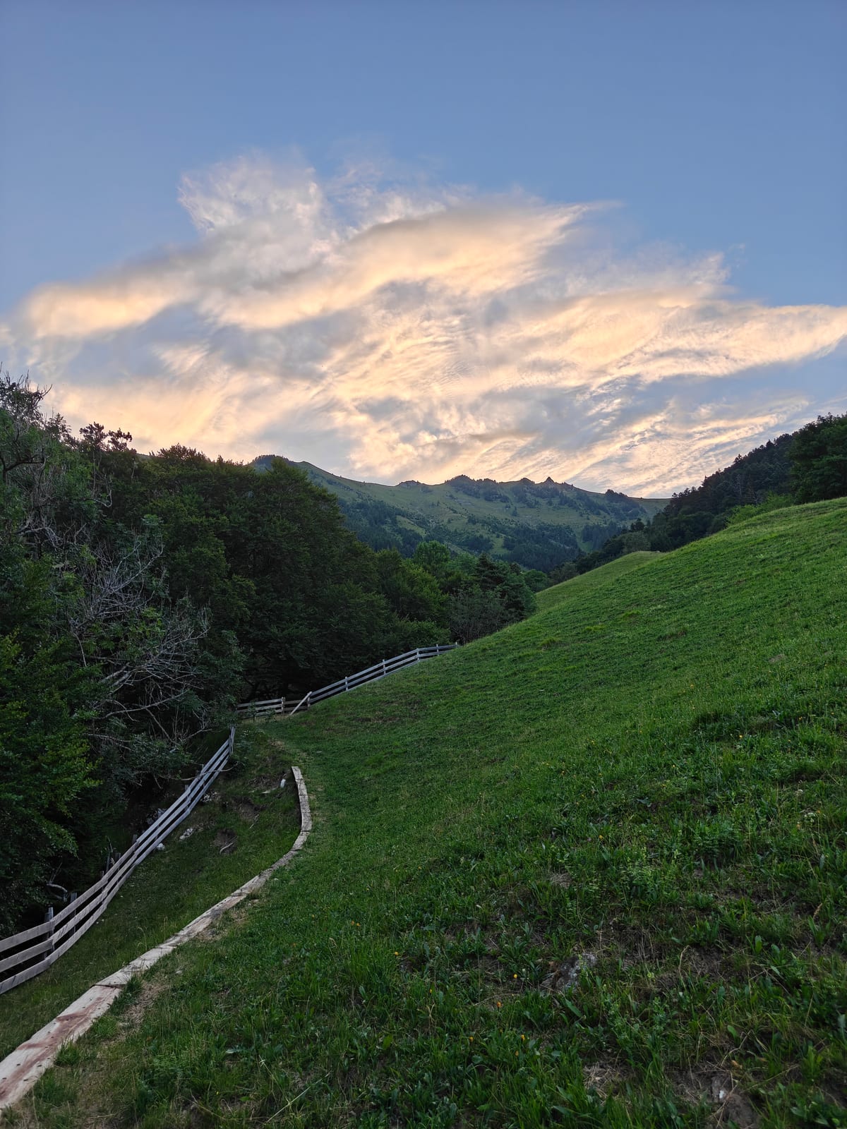 Wide rocky road climbing above St. Luziensteig, with a wooden fence and hills beyond