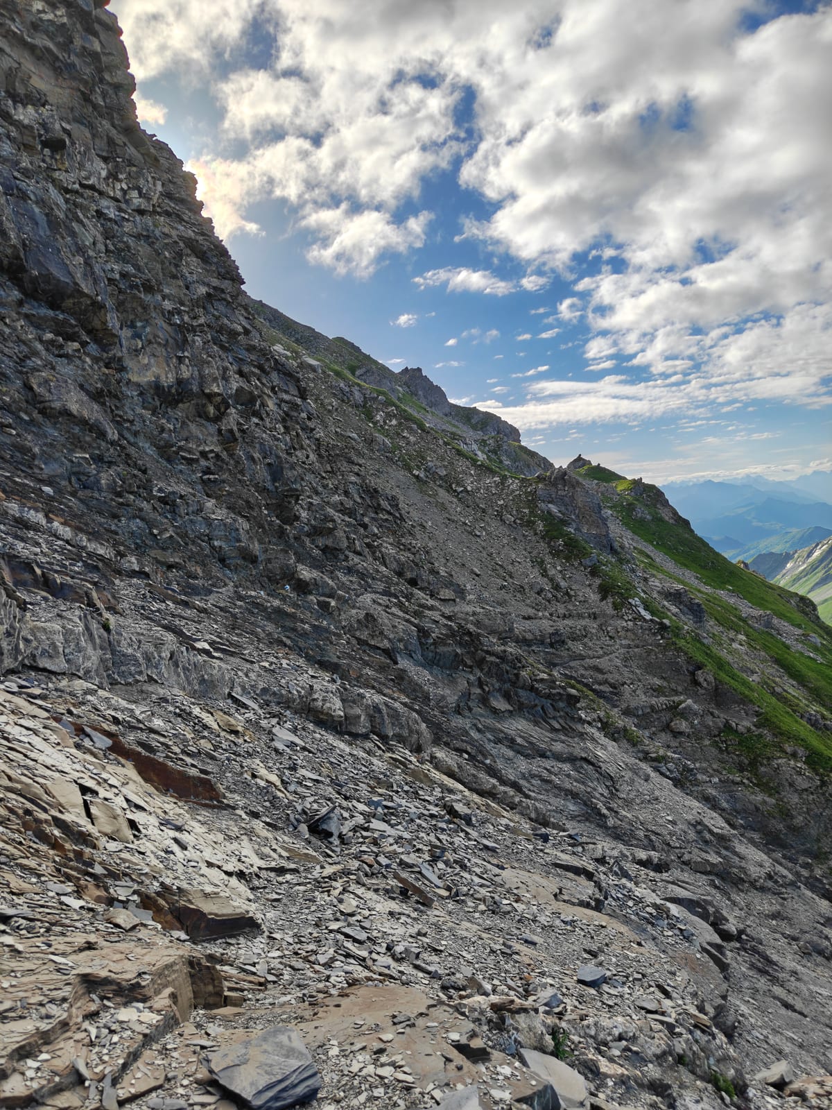 Trail crossing a wide, exposed slope of loose grey rock on the connecting ridge below Falknis