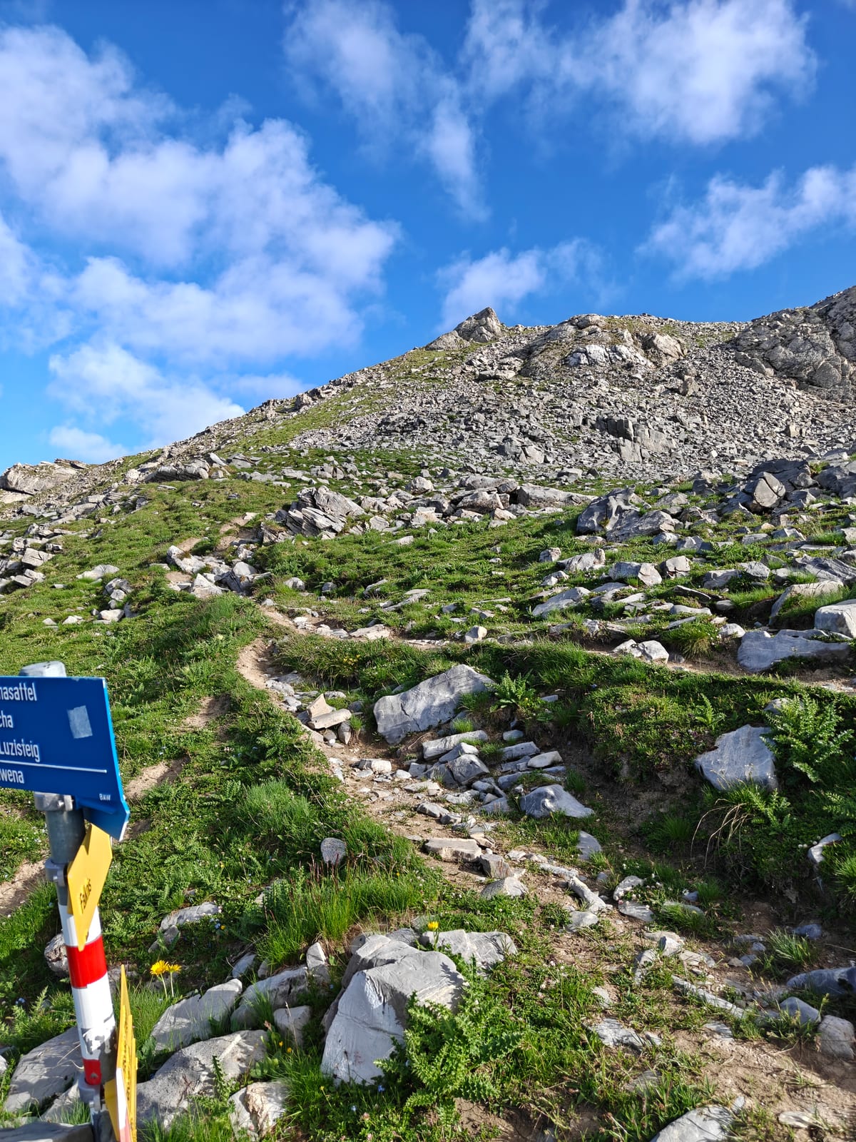 Trail signpost reading Guschasattel, Guscha, Luzisteig and Lawena, with a rocky summit trail continuing uphill