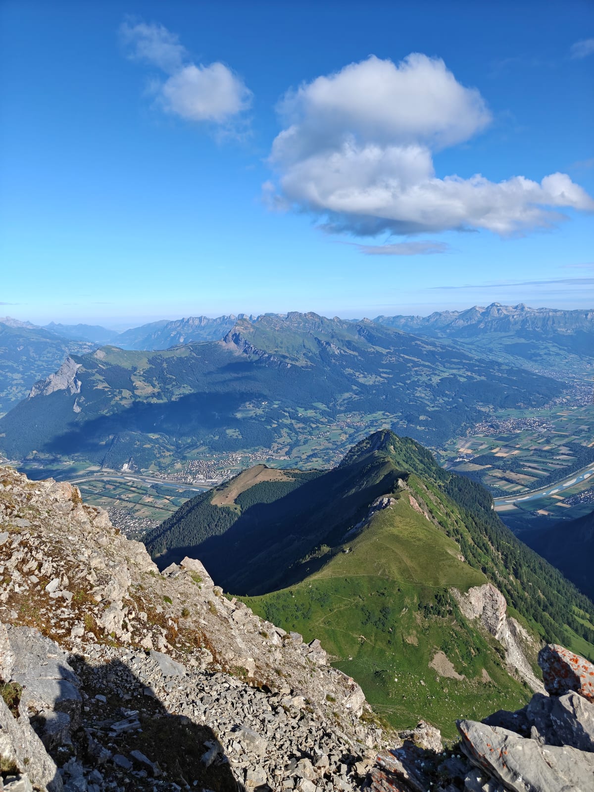 View south along a rocky and grassy ridge from the Falknis summit, with the Rhine Valley below